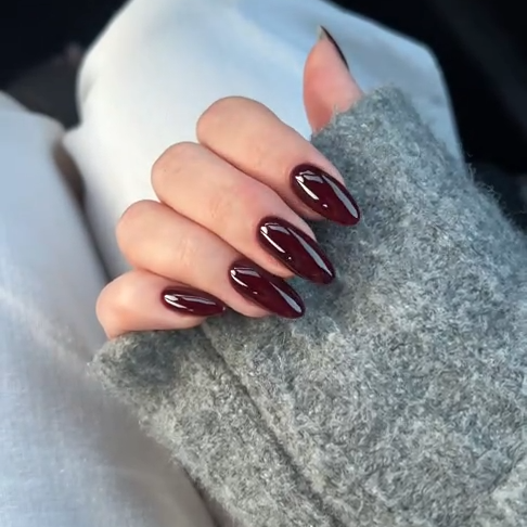Hand with dark cherry gloss nails wearing a gray textured sleeve.